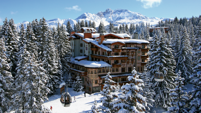 Snowy alpine trees surrounding Hotel Les Airelles with a snow capped mountain in the background.