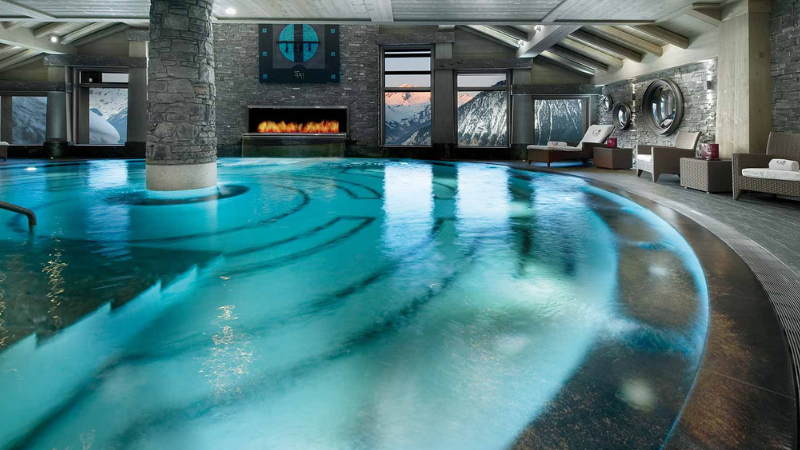 Oval shaped pool with a fire place and view of the sun setting over the mountains