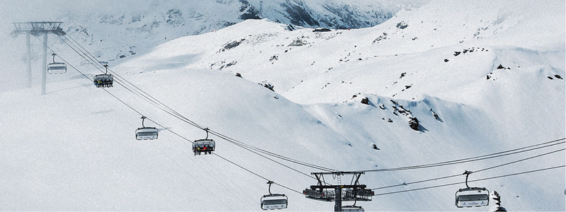 Snowy mountain side with cable car in foreground.