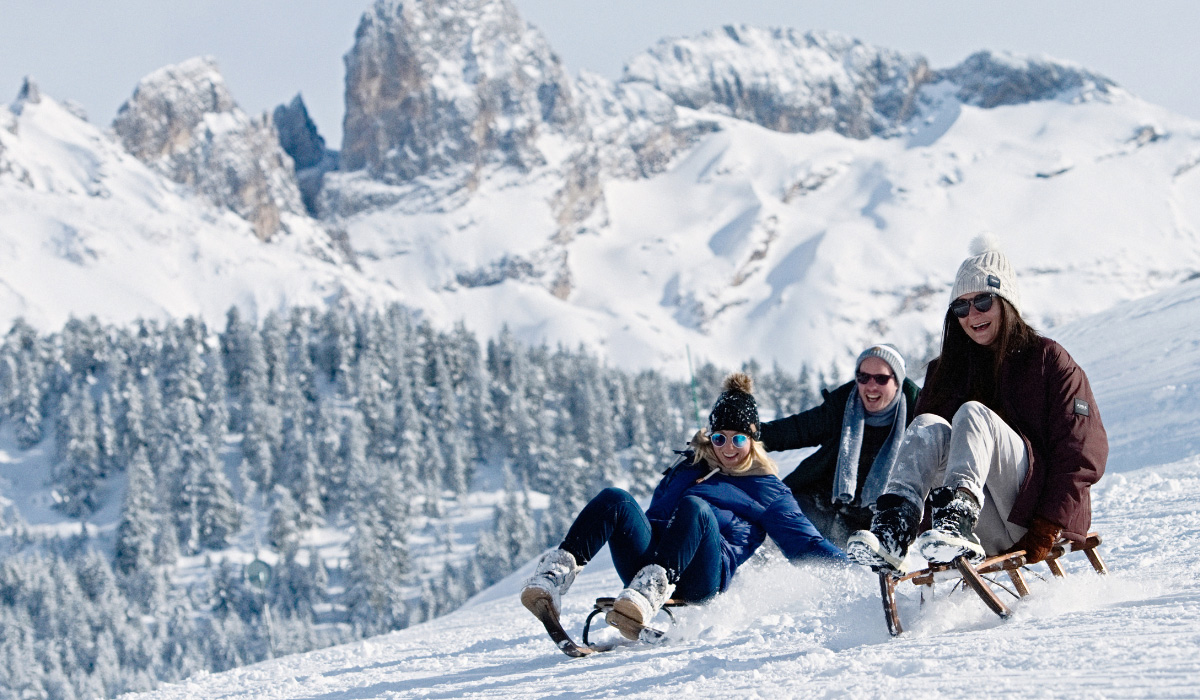 3 people sledging down snowy mountain