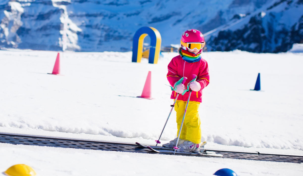 Girl Wearing A Pink Ski Jacket And Yellow Snow Trousers Skiing On A Slope