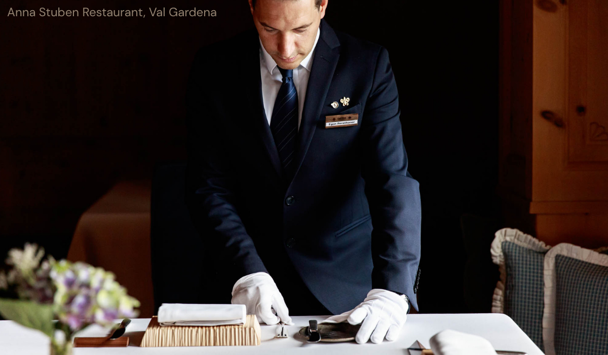 white gloved waiter/ matradee setting a white table clothed table.