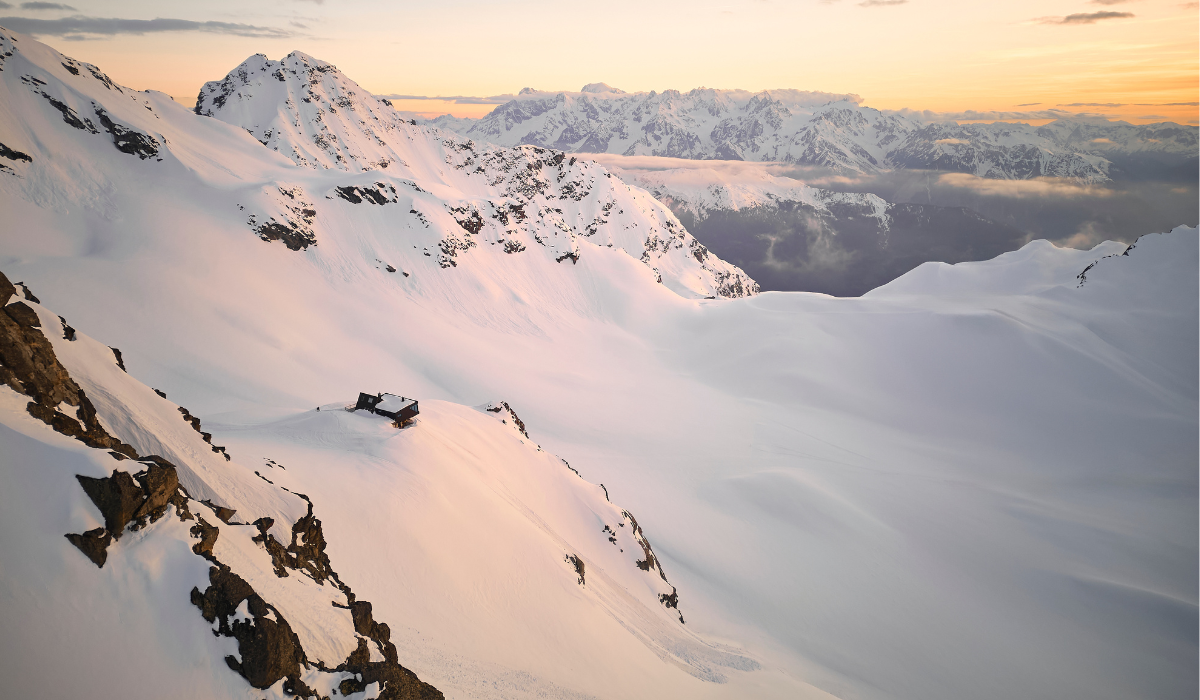 snow covered high mountain looking across the mountains with sun rising to the right.